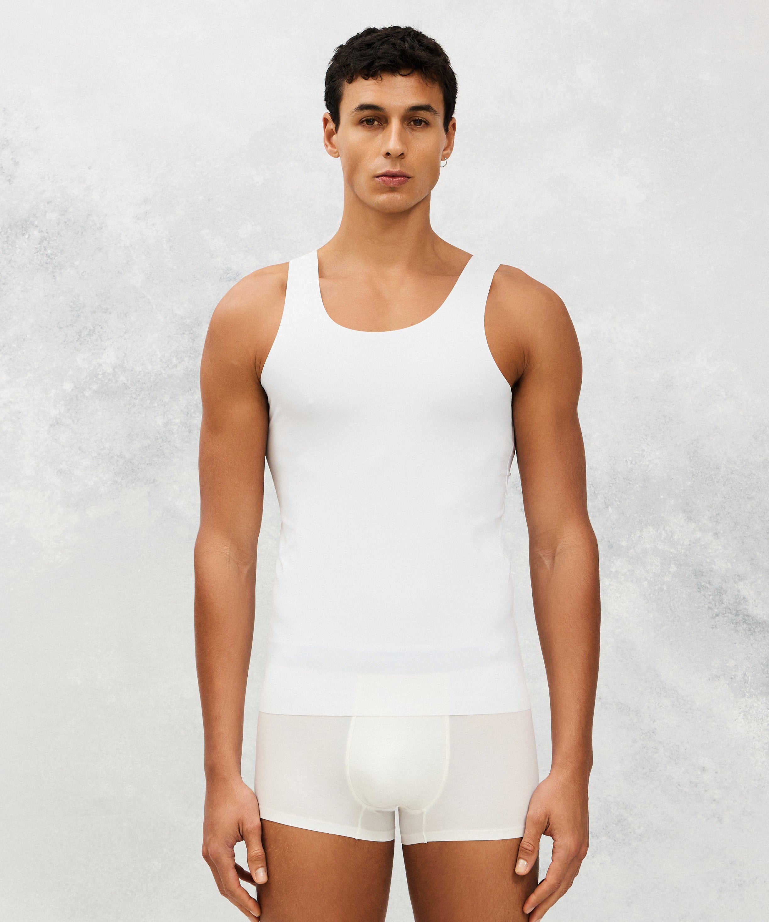 Person wearing a white tank top and shorts against a light gray background