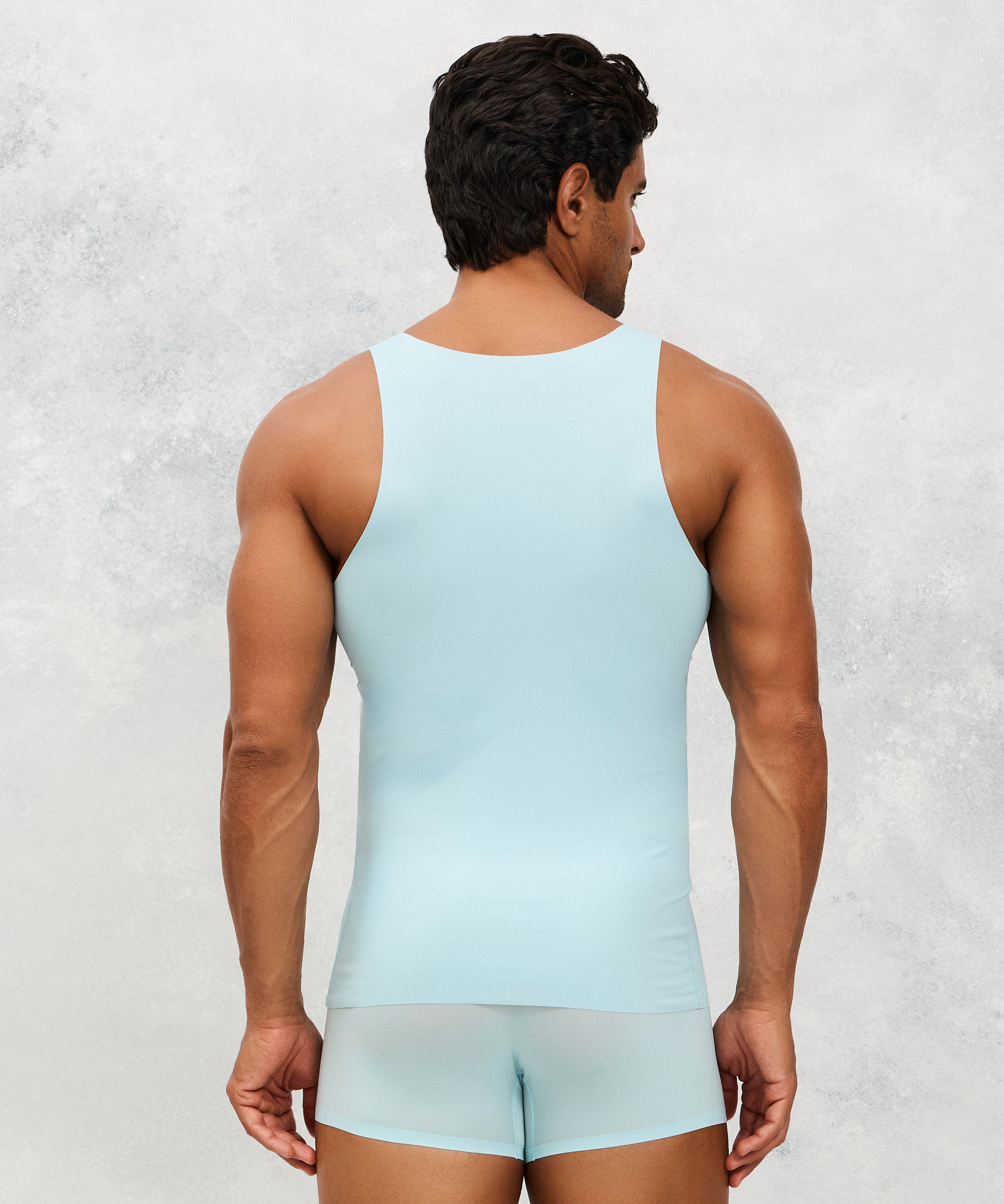 Man wearing a light blue tank top and underwear set against a textured white background