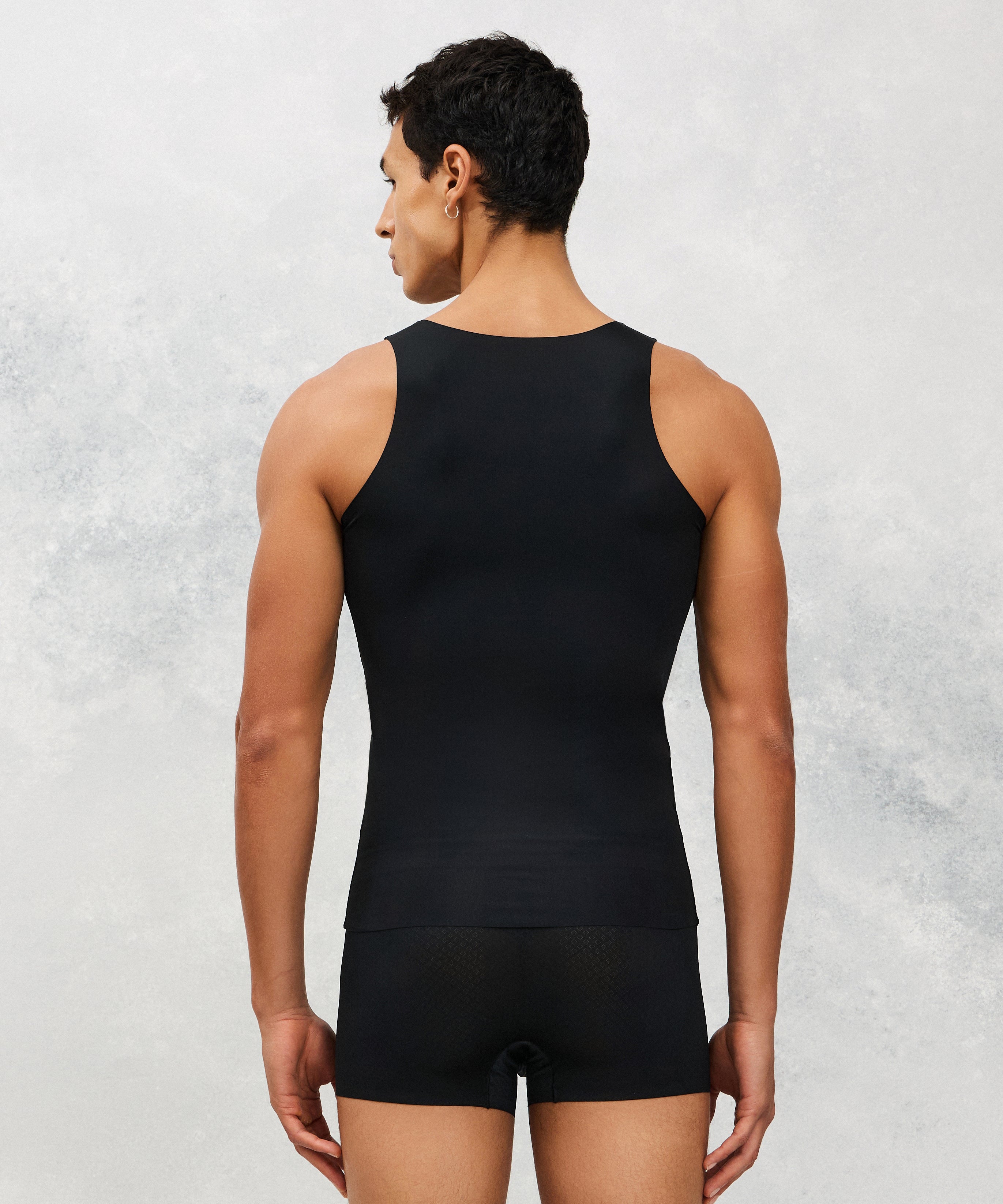 Person wearing a black tank top and shorts against a light gray background