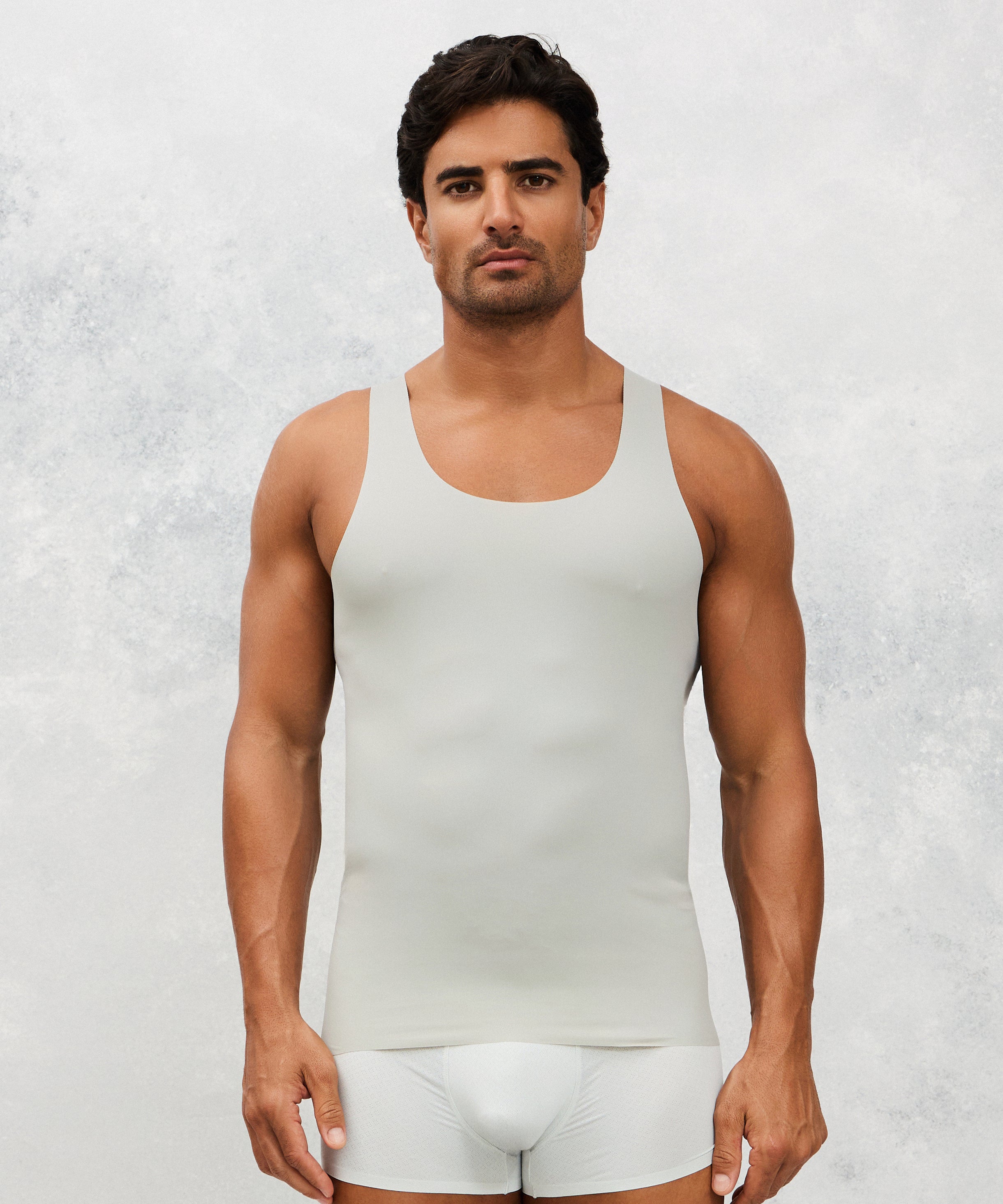 Man wearing a white tank top and underwear set against a light gray background